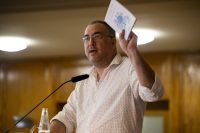 Bernardo Urbani speaking with a hand raised holding a leaflet